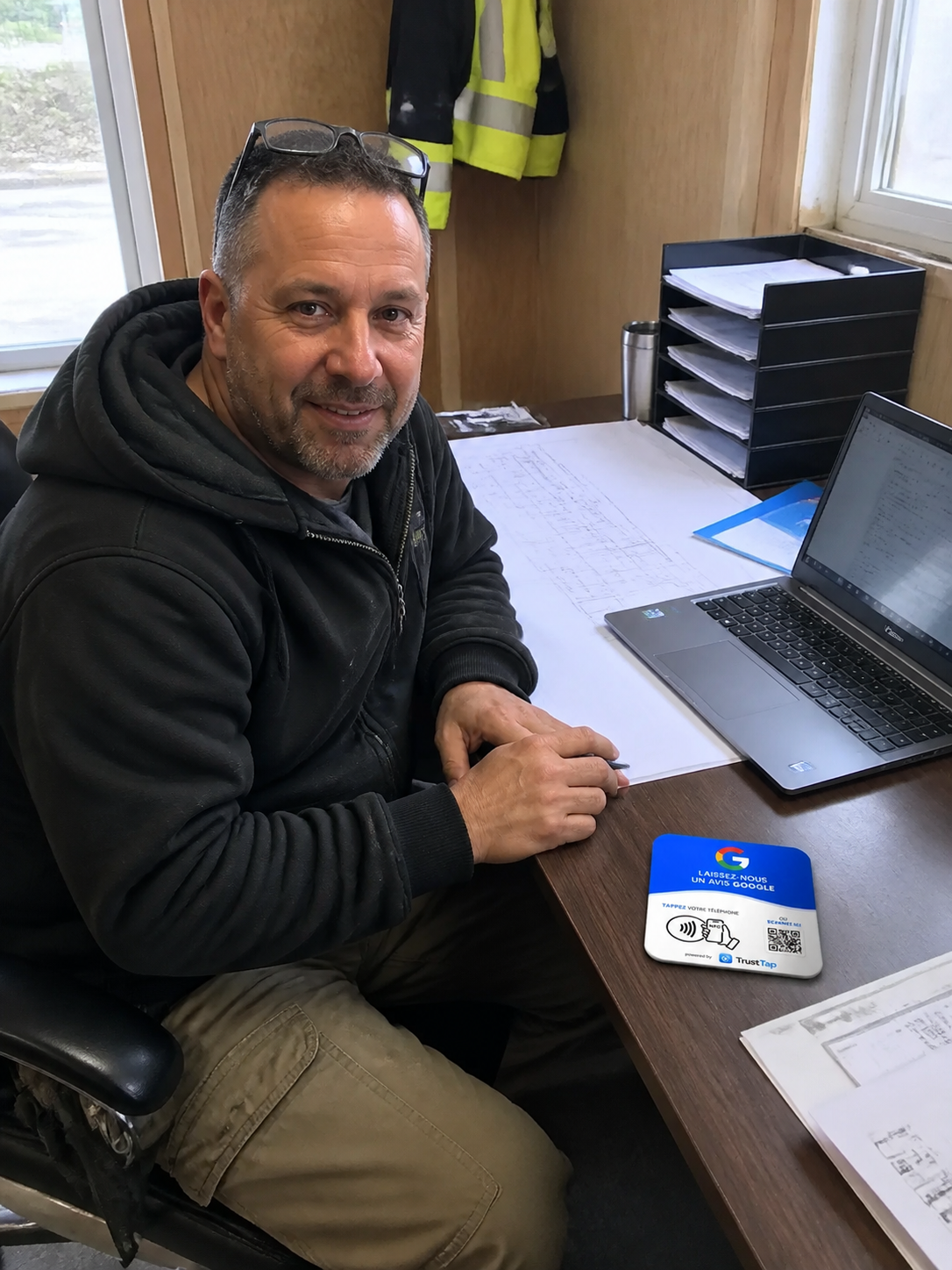 Entrepreneur général dans sa roulotte de chantier avec une plaque TrustTap de 12 par 12 centimètres posée à plat près de ses plans